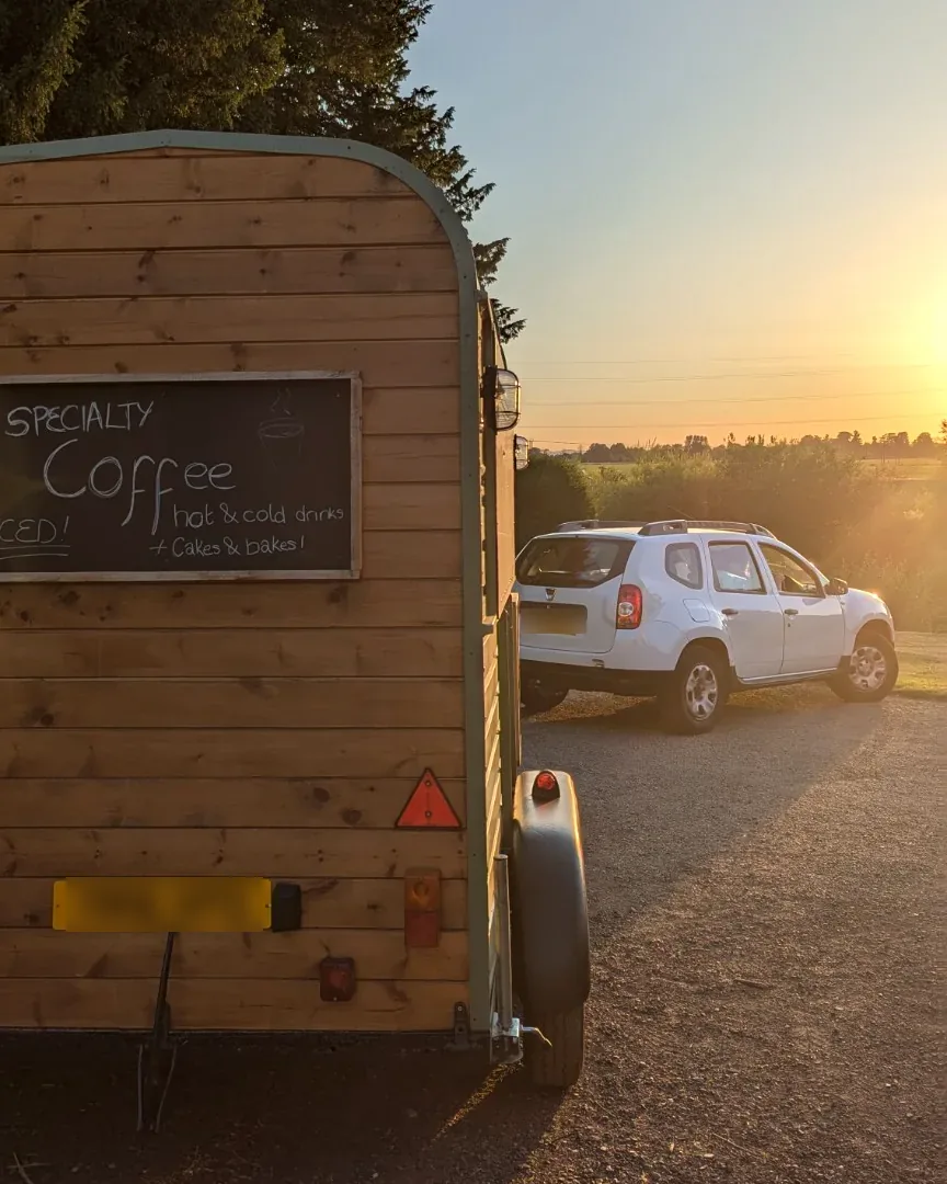 The Gallop & Grind horsebox hitched to its towing vehicle on a country track at sunset, chalkboard menu on the rear
