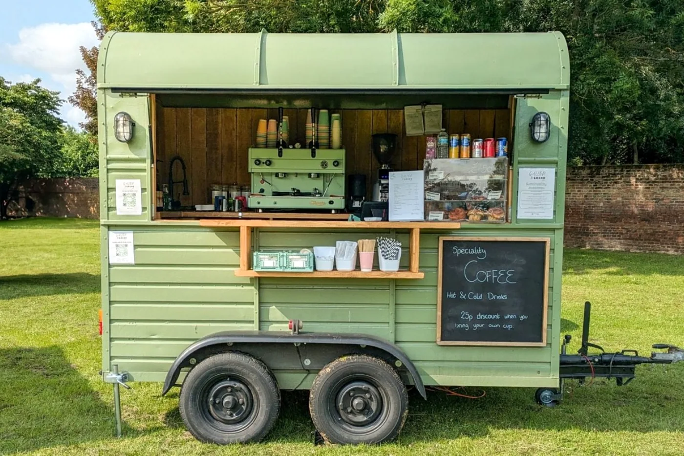 The converted Gallop & Grind horsebox on grass with the serving hatch open, espresso machine and chalkboard menu inside