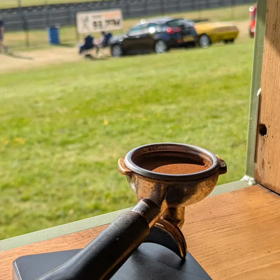 A dosed portafilter held up in front of cars at a motorsport event