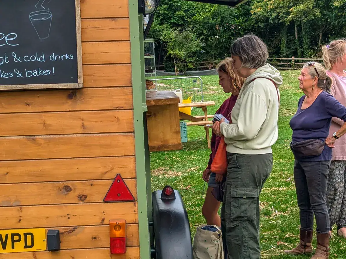 Guests queuing at the wooden rear of the Gallop & Grind horsebox on grass at a private outdoor gathering