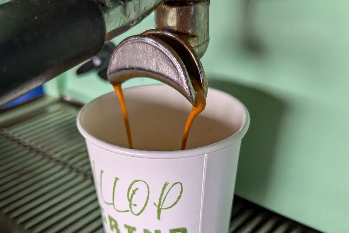 A double espresso pouring from the lever machine into a branded Gallop & Grind cup