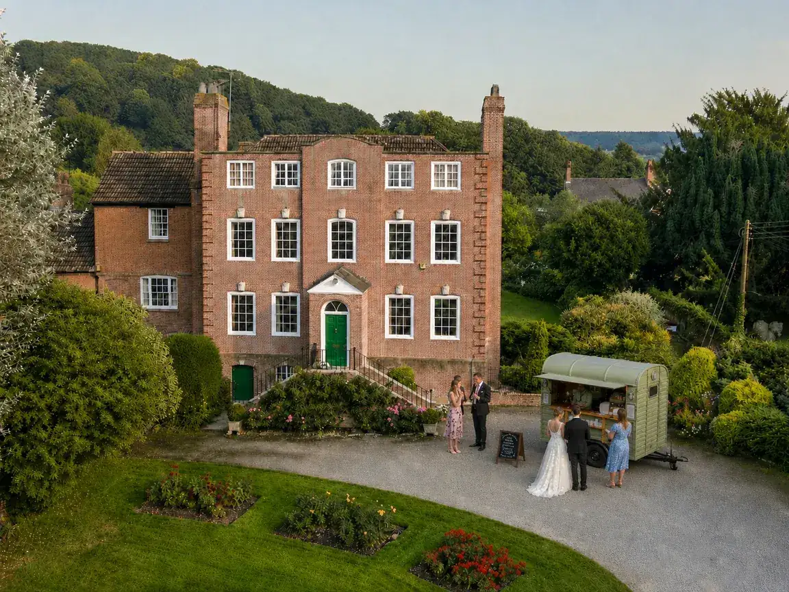 The Gallop & Grind horsebox serving coffee to a bride, groom and guests outside a red-brick country house.