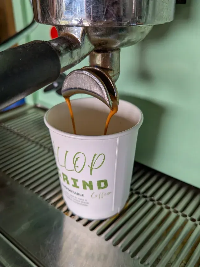 Fresh espresso pouring into a Gallop & Grind branded compostable cup from the Astoria lever machine.